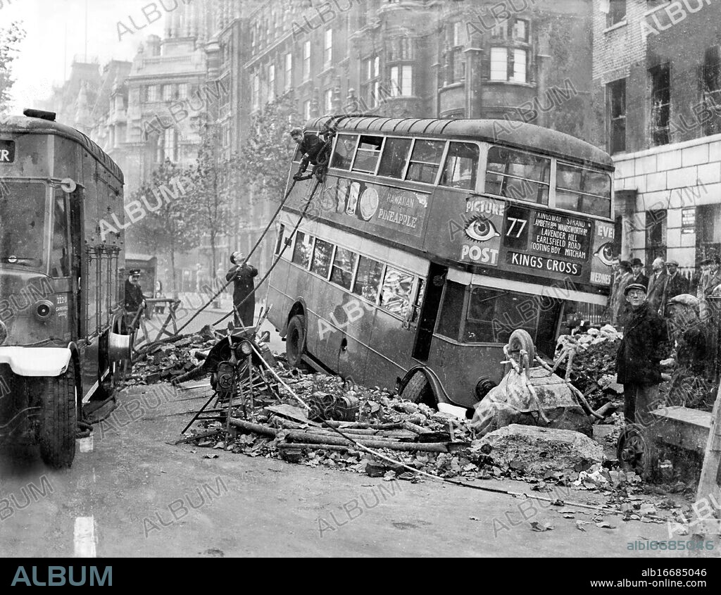 London transport workers try to retrieve a bus that had sunk into a hole when the road beneath it collapsed following a night of heavy bombing. United Kingdom 1940.