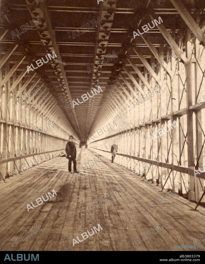 Interior of the Niagara Falls Suspension Bridge, which stood from 1855 to 1897 across the Niagara River, was the world's first working railway suspension bridge. It spanned 825 feet (251 m) and stood 2.5 miles (4.0 km) downstream of Niagara Falls, where it connected Niagara Falls, Ontario, to Niagara Falls, New York. Trains used the upper of its two decks, pedestrians and carriages the lower. One frame of stereoscopic image by George Barker (1844-1894).