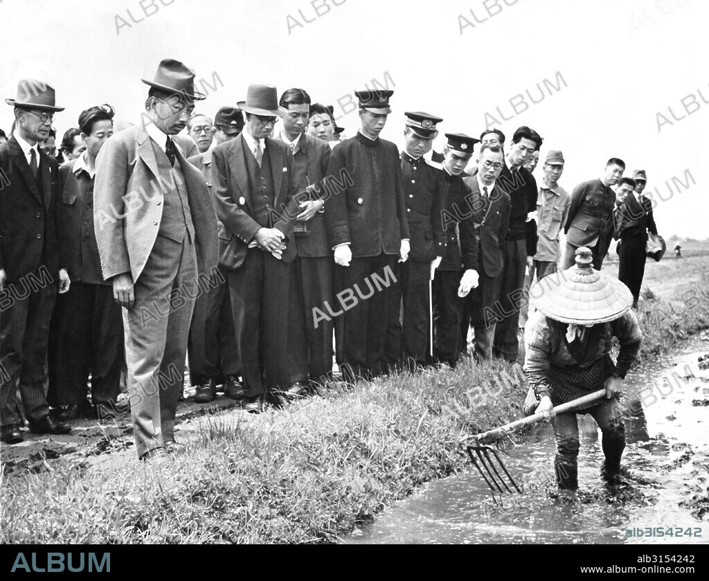 Japan:  March 19, 1948 Emperor Hirohito visits the farming communities to learn first hand the problems they are having. Here he watches a farmer till a rice paddy with a crude spade.