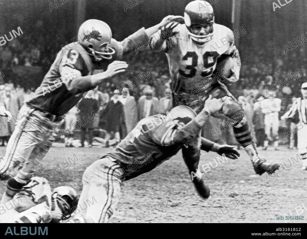 Detroit, MIchigan: December 10, 1961. Minnesota Vikings running back Hugh McElhenny (39) leaps but cannot avoid being tackled by Detroit Lions players, Gary Lowe (43) and Dick LeBeau during a National Footbal League game.