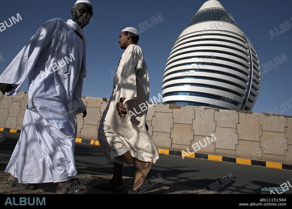 Locals walk past the 5-star Boji Al-Fateh Hotel (Libyan Hotel), designed to represent a sail, Khartoum, Sudan, Africa.