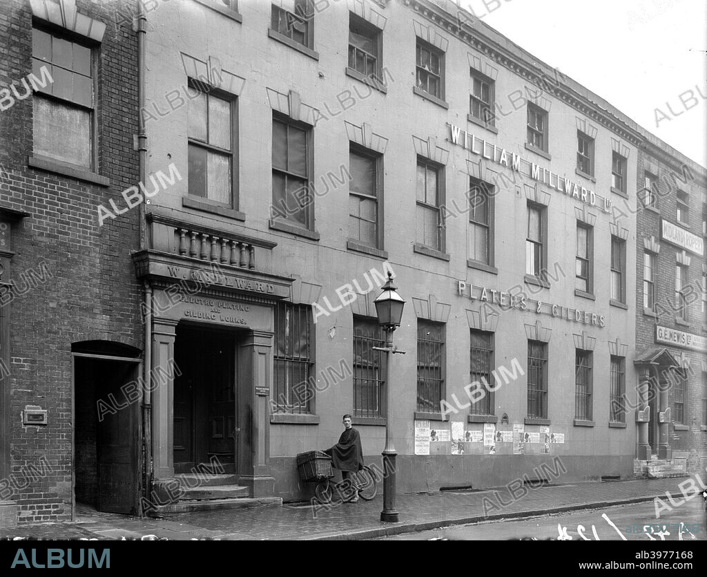 William Millward Ltd, Birmingham, West Midlands, 1940s. A delivery boy leans his bicycle against the wall of number 37 St Pauls Square, Birmingham, the workshop of William Millward Ltd, a plater and gilder. The terrace may originally have been built as town houses circa 1780. By the time this photograph was taken in the 1940s they were undoubtedly used for industrial purposes.