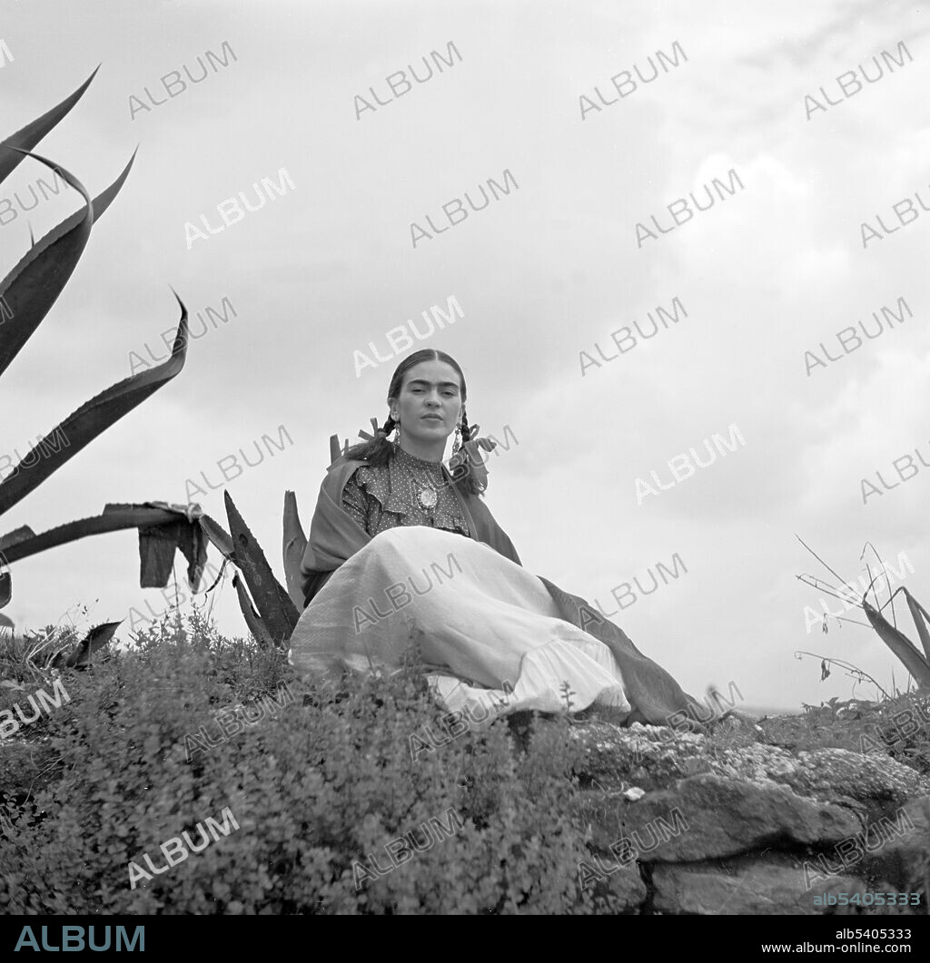 Kahlo, seated next to an agave plant, during a photoshoot for Vogue magazine, Senoras of Mexico. Frida Kahlo de Rivera (1907 - 1954) was a Mexican artist. During the late 1920s and early 1930s, she developed her own style as an artist, drawing inspiration from Mexican folk culture, and painting mostly self-portraits which mixed elements from pre-Columbian and Catholic mythology.  Photographed by Toni Frissell, 1937.