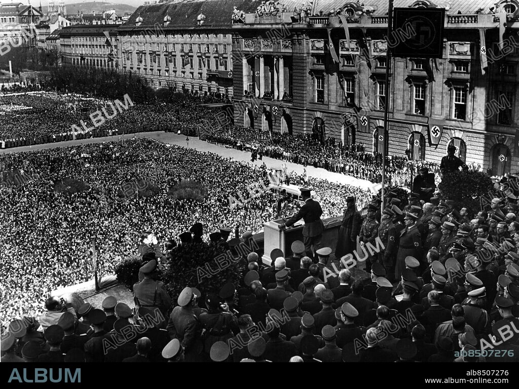 Orig. bildtext... ADOLF HITLER VERKÜNDETE DAS AUFGEHEN OESTERREICHS IM DEUTSCHEN REICH. In einem feierlichen Staatsakt verkündete der Führer und Kanzler der deutschen Nation und des Deutschen Reiche vor einer riesigen Menschenmenge von der Rampe der Hofburg in Wien den Eintritt seiner Heimat in das Deutschen Reich. In seiner Ansprache umriss er die Bedeutung der ältesten Ostmark des deutschen Volkes. U.B.z. Adolf Hitler während seiner Rede und einen Teil der riesigen Volkmenge auf dem Heldenplatz vor der Hofburg. Etwas weiter rechts sieht man Stabschef Lutze und Reichsleiter Rosenberg und ferner (in Zivil) den nunmehrigen Reichsstatthalter Dr. Seyss-Inquart. Anm. Anschluss persons: Adolf Hitler ;Alfred Rosenberg ;Arthur Seyss-Inquart sites: TYSKLAND* ;WIEN ;ÖSTERRIKE.