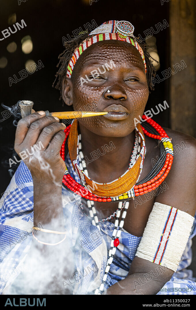 Woman with beauty scars from the Toposa tribe smoking a pipe, Eastern Equatoria, South Sudan, Africa.