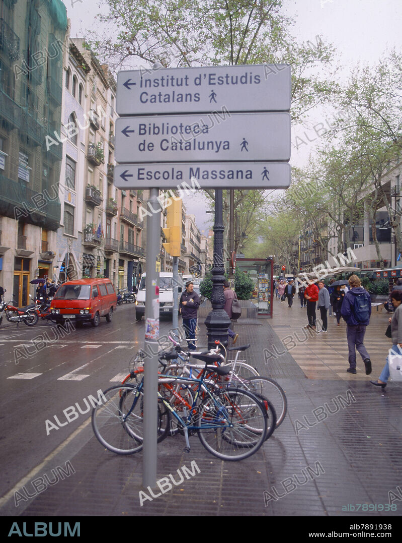 CARTEL INDICATIVO CON LAS DIRECCIONES ESCRITAS EN CATALAN- BICICLETAS APARCADAS.