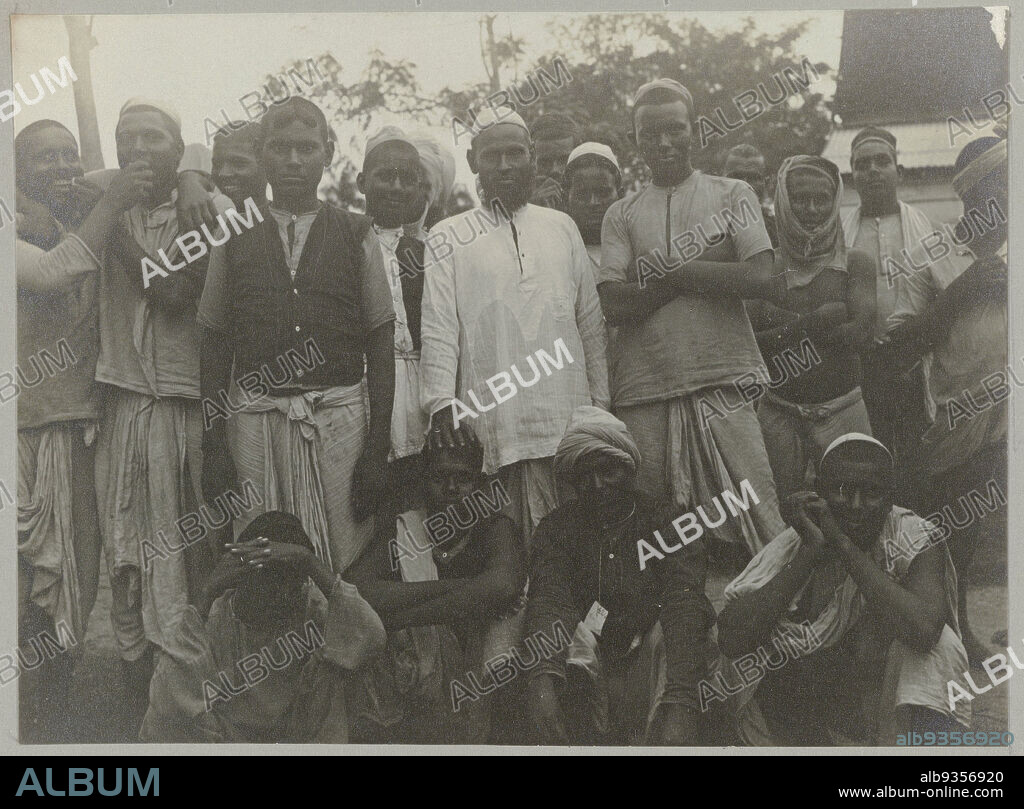 Hindustani contract workers in the immigrant depot, In the coolie depot (title on object), A group of contract workers from the British East Indies, in the so-called 'coolie depot', the central gathering point for immigrants in Paramaribo. Part of the photo album Souvenir de Voyage (volume 5), about the life of the Doijer family in and around the plantation Ma Retraite in Suriname in the years 1906-1913., Hendrik Doijer (attributed to), Suriname, 1906 - 1913, photographic support, gelatin silver print, height 82 mm × width 112 mm.