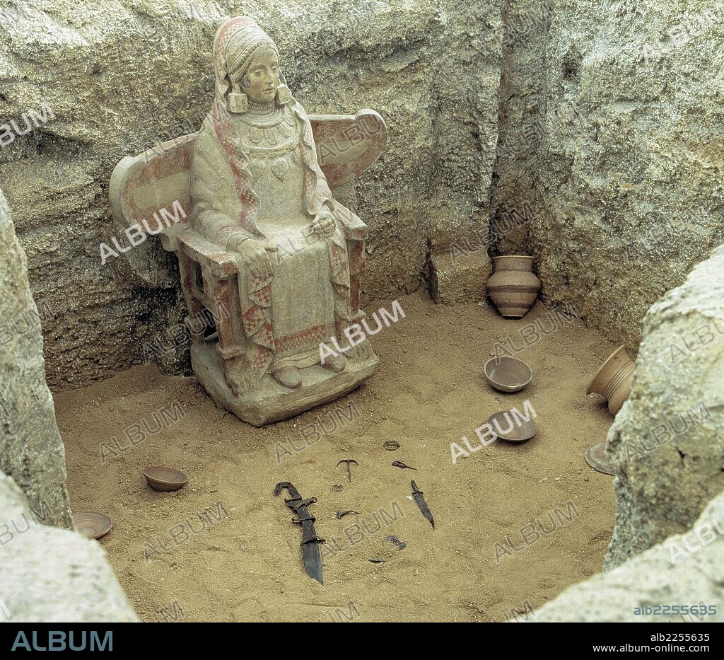 DAMA DE BAZA. ARTE IBERICO. Escultura ibérica labrada en piedra con policromía, muy bien conservada, hallada en el Cerro Cepero cerca de Baza. Representa una deidad femenina sentada que se encontró en el interior de una tumba en la que servía de urna ci- neraria. Reconstrucción de su hallazgo en la Exposición de ARTE IBERICO (Madrid, 1983).