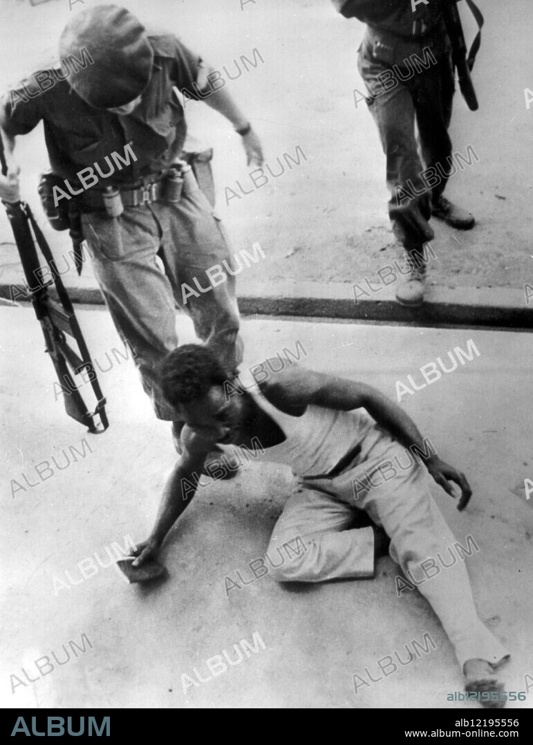 Helping Kick For A Rebel, Stanleyville, Congo. A Congolese rebel - a "Simba" - is given a helping kick along by a white mercenary after he was arrested, 25th November 1964, in the mopping-up operations after the 24th November massacre.