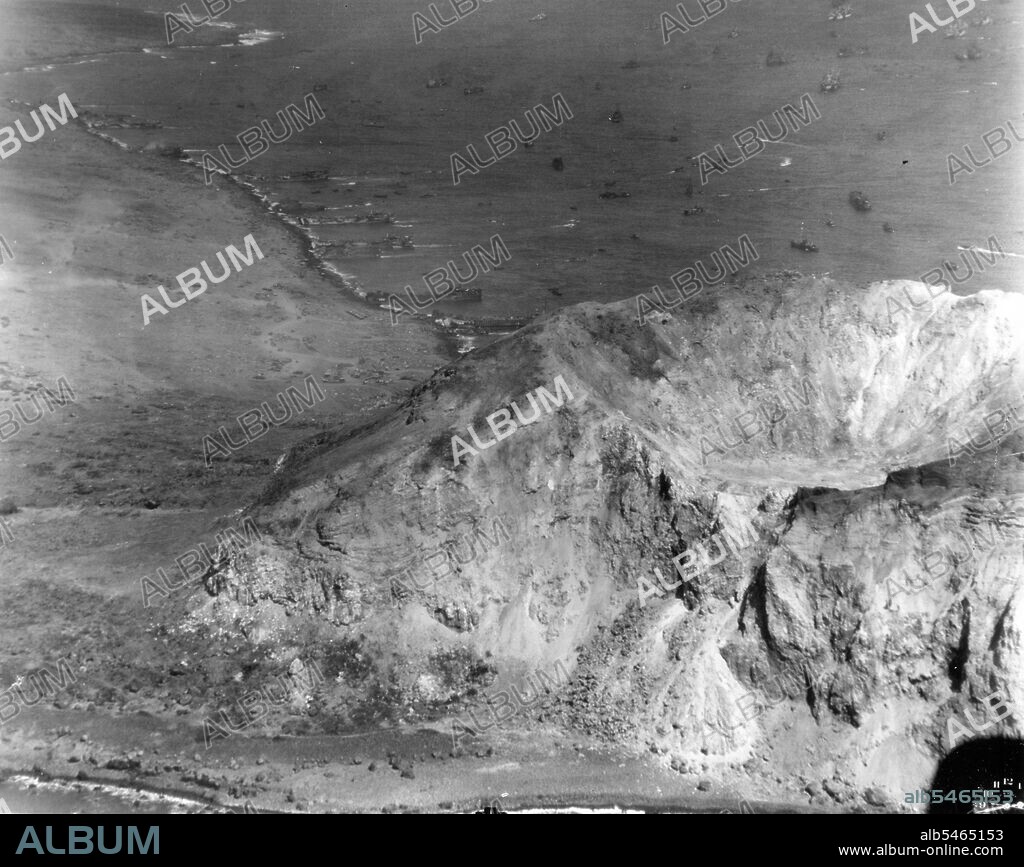 Aerial of Mt. Suribachi, Iwo Jima, Volcano Island. Alt 500'. Taken from a plane from USS MAKIN ISLAND (CVE 93). LSTs and landing craft at beach in background.