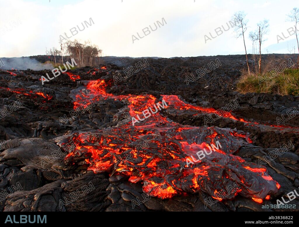 Lava breaks out of a channelized Aa flow on Kilauea volcano in Hawaii. The new lava, transitional in nature betwen pahoehoe and Aa lava is flowing over older phahoehoe flows and smooth pahoehoe surrounding the channel. Also note the vegetation near the lava flow. Seeds from this island of life (called a kipuka) will help the cooling land return to life.