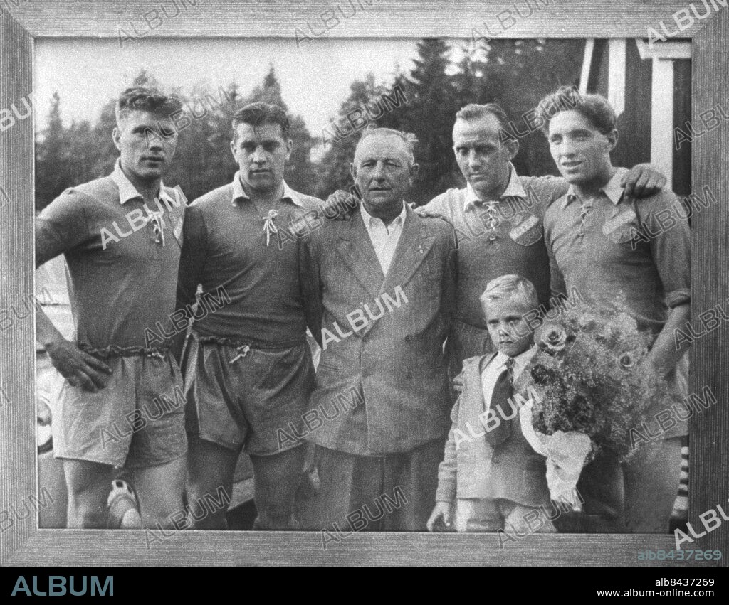 ©SCANPIX SWEDEN, 1983-08-30.. Bröderna Nordahl inom glas och ram.. På väggen hänger ett foto från förr. Vi ser pappa Emil Nordahl i mitten i kostym med sina söner (fr.v.) Göran, Gunnar, Bertil och Gösta, alla i sportkläder. Knut var sjuk. Lillgrabben är Thomas Nordahl, Gunnars pojke.. Foto: Scanpix. Code: 20360. Nordahl brothers, footballplayers.