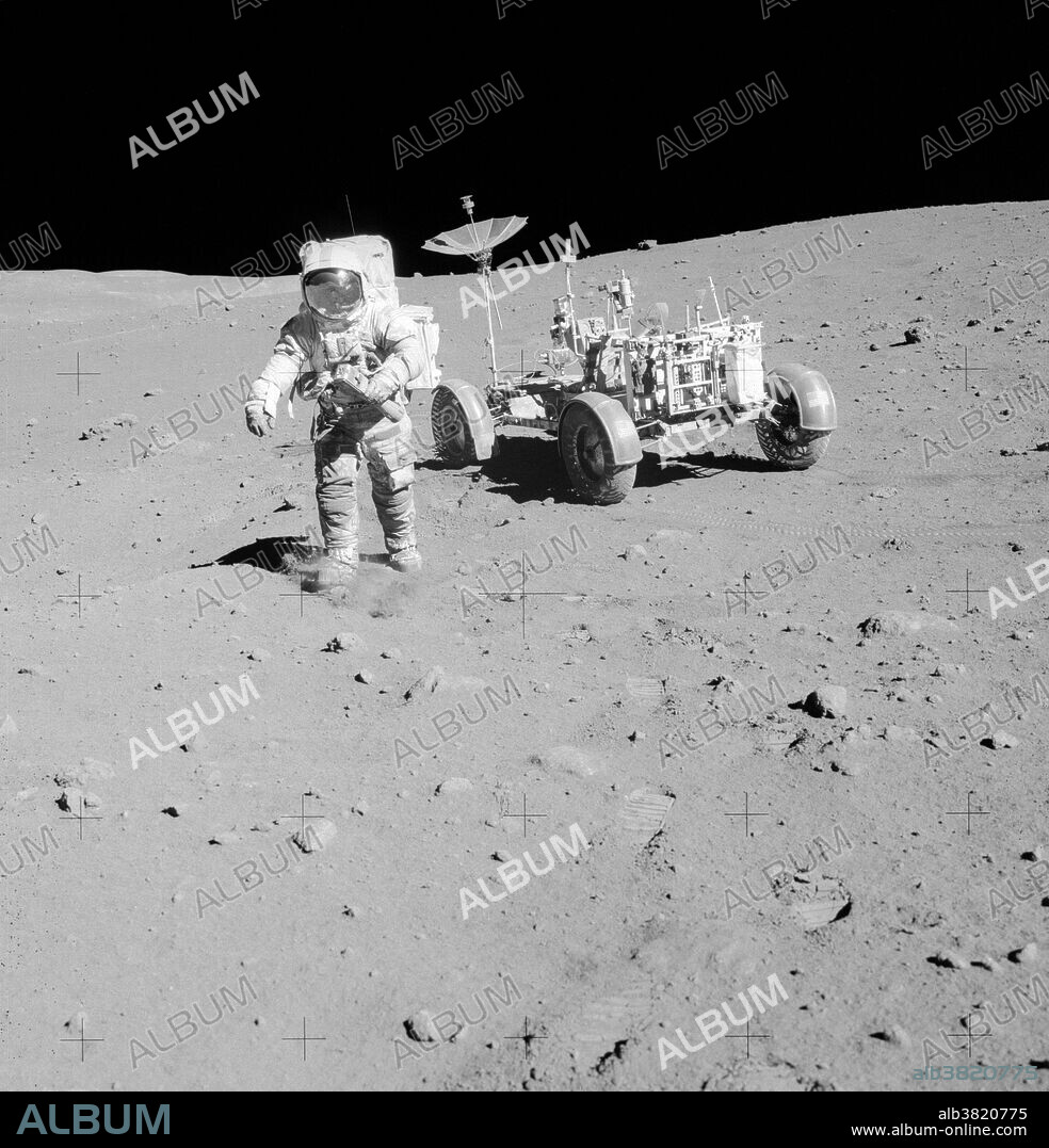 Astronaut David R. Scott, Apollo 15 commander, walks away from the Lunar Roving Vehicle (LRV) during the third and final Apollo 15 lunar surface extravehicular activity (EVA-3) at the Hadley-Apennine landing site on August 2, 1971. The LRV is parked a short distance from the rim of Hadley Rille. The far wall of the rille is in the distant background at extreme upper left. In his left hand, Scott is holding a 70mm camera equipped with a 500-mm lens. The photograph was taken by astronaut James B. Irwin, lunar module pilot. While astronauts Scott and Irwin descended in the Lunar Module (LM) to explore the moon, astronaut Alfred M. Worden, command module pilot, remained with the Command and Service Modules (CSM) in lunar orbit.
