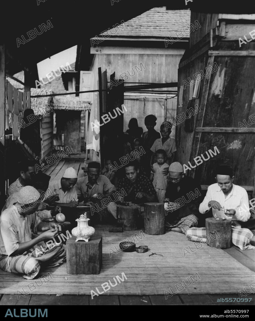 The River Kampong: A group of silversmiths at work in a house in the Brunei river Kampong. Malays build their houses on stilts, a simple and straightforward hut. In the whole of Malaysia you can tell a Malay house from a Chinese or an Indian one by its stilts. True the Sakai in Malaya and the Iban tribes of Borneo put their houses off the ground but they are different again. In Brunei town the Malays have gone one better, they have built their town in a river. Ten thousand men, women and children are born, live and die, eat and sleep over the water. The men are fishermen, and as fishermen the men and boys see something of the rest of the world; but the women are in a sense prisoners, doubly imprisoned by religious convention and the water of the Brunei river. May 01, 1950. (Photo by British Official Photograph).