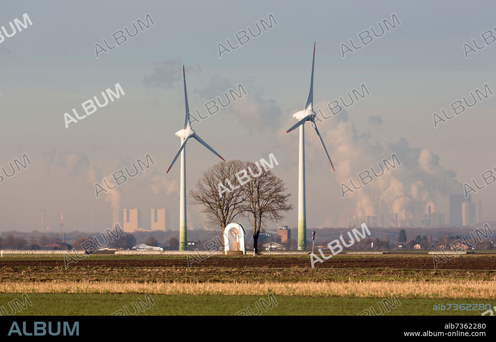 von zwei Linden flankierter Bildstock aus dem 18. Jahrhundert, dahinter zwei Windkraftanlagen und Kohlekraftwerke (Rheinisches Braunkohlerevier).