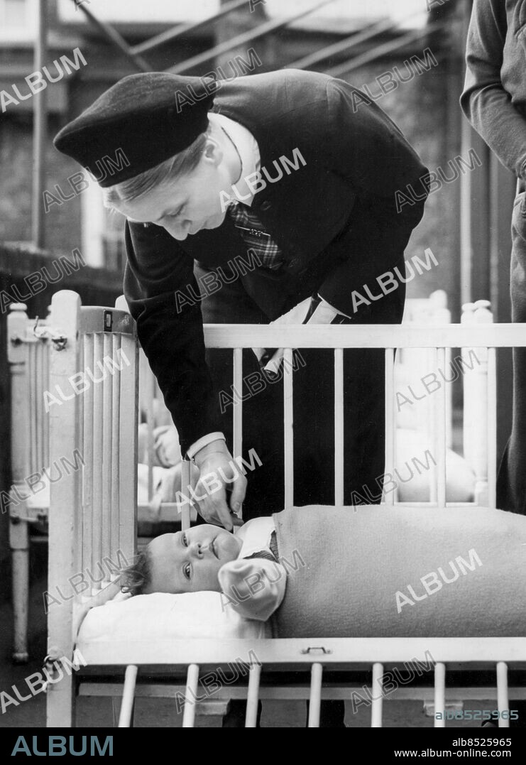 Orig. bildtext... NAZI WOMEN'S LEADER VISITS HOSPITAL OF MOTHERCRAFT TRAINING SOCIETY. 8.3.39. Frau Gertrud Scholtz-Klink, Nazi women's leader who is on a four-day visit to London, this morning visited Cromwell House, hospital of the Mothercraft Training Society. O.P.S. Frau Scholtz-Klink admiring and making friends with one of the little inmates at the training centre this morning. Anm. G Scholtz-Klink, 1902-1999, tysk ledare för de organiserade nazistiska kvinnorna, från 1934 Reichsfrauenführerin. Klappa Spjälsängar Bebisar Barnsjukhus Barnavårdsträning CD575 persons: GERTRUD SCHOLTZ-KLINK sites: TYSKLAND*;LONDON;STORBRITANNIEN.