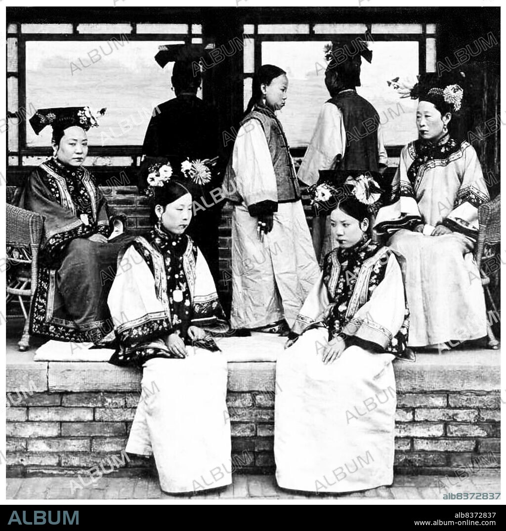 Manchu women of the Forbidden City or Gugong in Beijing pose for a photograph c. 1910 in the very last days of the Manchu Qing Dynasty (1644-1911). They wear elaborate and expensive dresses. Their faces are whitened with powder, and their lipstick is applied in a narrow band across the centre of their lips following the fashion of the time.
