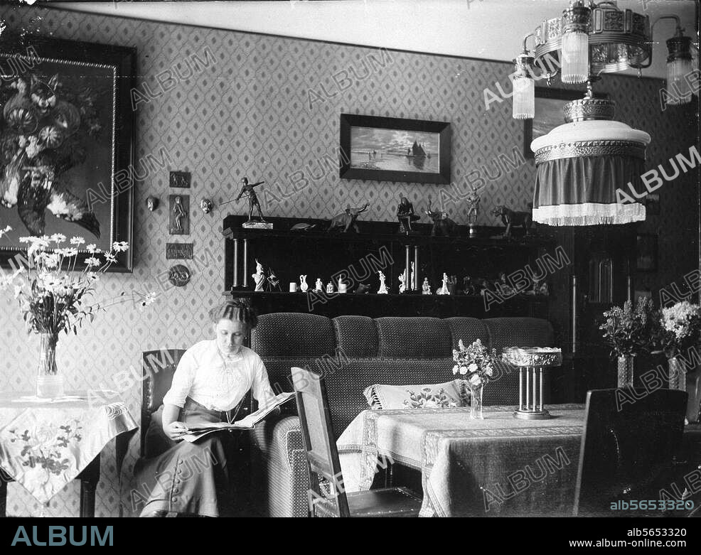 Wohnung:. Wohnzimmer. Bürgerliches Wohnzimmer mit Frau, in einem Fotoalbum blätternd. Foto, Berlin 1913.