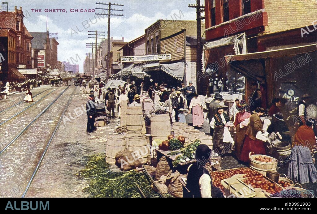 The ghetto, Chicago, Illinois, USA, 1910. Postcard view of Chicago's ghetto showing a street scene of open air vendors with their goods spread out along the curbs. Many people are seen milling about. Street car tracks run down the middle of the street.