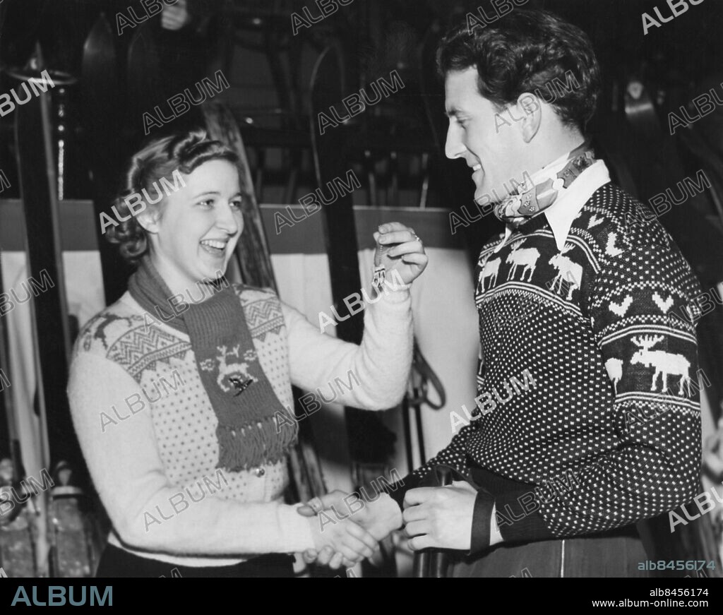 Orig. bildtext... A WEE BIT SMALL BUT THEY'RE LUCKY. NEW YORK CITY - Ella Gulbrandsen, who is Norway's outstanding girl ski jumper at the age of 17, presents Tomm Murstad, leading Norwegian ski instructor, with a pair of abbreviated mittens after finding that the Winter Sports Show in Madison Square Garden kept her so busy that she couldn't knit Murstad the full-sized pair she had promised him. The tiny gloves are worn for luck in Norway and Murstad was well pleased. Anm. Lusekofter Stickat Handslag Presenter Gåvor Leenden Profiler Visa Halsdukar Scarfes Mönster Älgar Tonåringar Vantar Talismaner Stickade tröjor Mönsterstickat Maskots persons: TOMM MURSTAD;ELLA GULBRANDSEN sites: NEW YORK;NORGE*;USA.