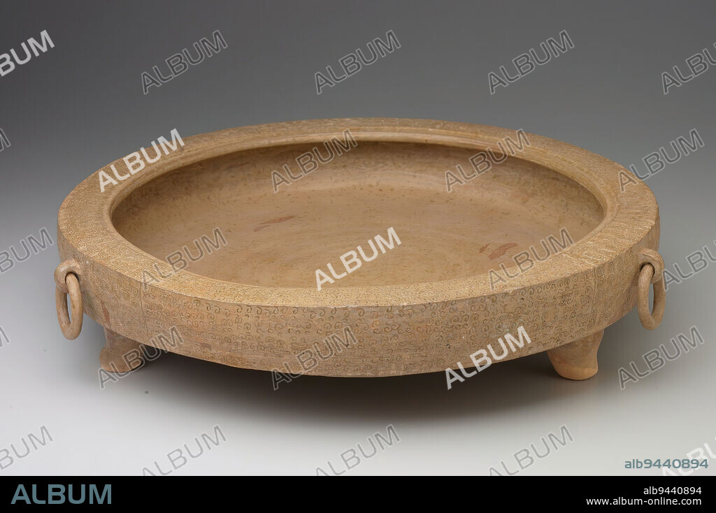 Tripod Basin (pan), 6th-5th century BCE, 3 7/8 x 17 1/4 x 17 11/16 in. (9.8 x 43.8 x 44.9 cm), High-fired stoneware with incised designs under a light yellow-green glaze, China, 6th-5th century BCE, This shallow round basin is hand-built from clay coils and is very heavily potted. The vessel closely follows the shape of bronze tripod water basins of the Eastern Zhou period (770-221 BCE). The outside has three animal masks holding loose rings similar to the bronze vessels it imitates. The broad rim and exterior are decorated with stamped spiral designs also in vague imitation of late Zhou bronze decoration.