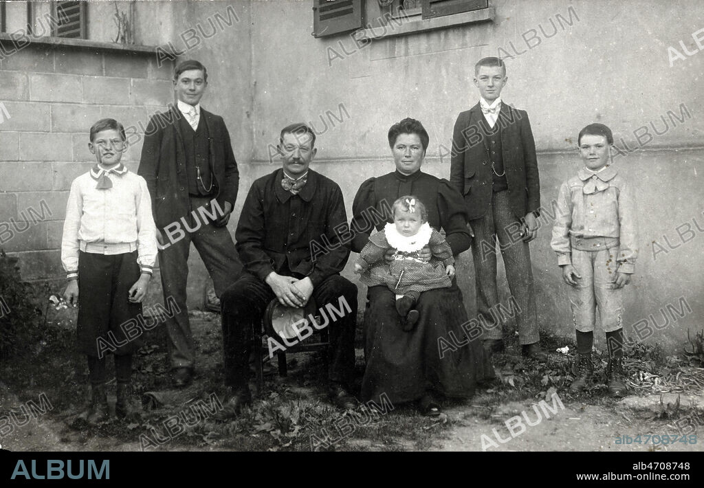 FAmille nombreuse d'origine modeste, famille ouvriere. 5 enfants dont le dernier ne sur les genoux de la mere. Le pere en costume d'ouvrier a ote sa casquette. 4 garcons, les 2 grands arborent fierement leur chaine de montre. Carte postale photographique. Credit COllection KHARBINE TAPABOR.