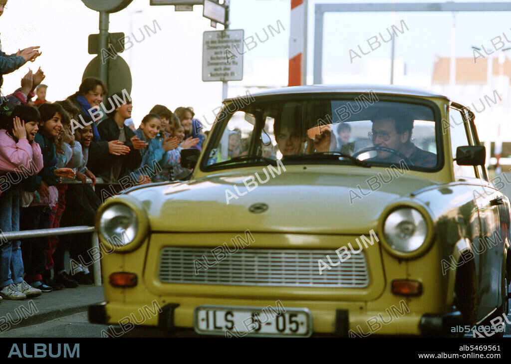 West German children applaud as an East German couple drive through Checkpoint Charlie and take advantage of relaxed travel restrictions to visit West Germany..