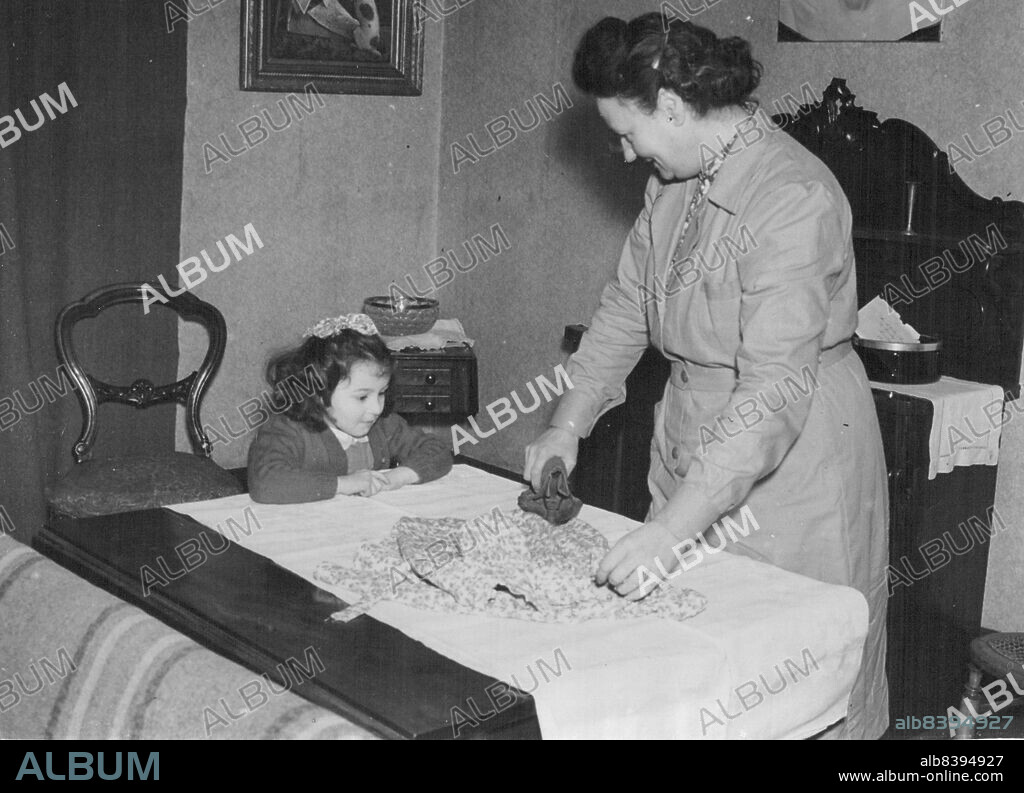Tania Prepares To Go To The Palace -- Tania watches Mrs. Bushell, her grandmother, ironing the dress she will wear when she goes tot he Palace tomorrow (Tuesday). The painting on the war in of her mother.Tania Szabo, four-year-old daughter of Madame Violette Szabo, who was awarded the G. C. for ***** service work during the war, prepares to got to the Palace to receive the model awarded to her mother. January 27, 1947. (Photo by Keystone).