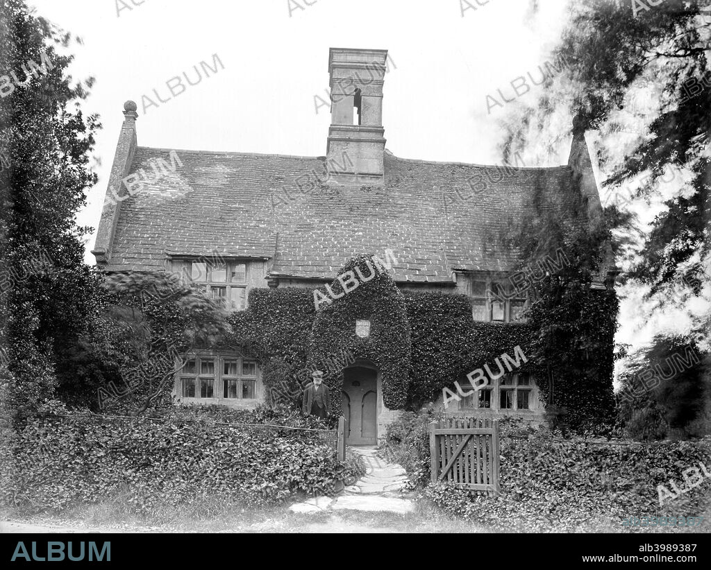 Haunt Hill House, Weldon, Northamptonshire, 1928. Entrance front of Haunt Hill House, Weldon, which is dated to the 1630s-40s. Foliage has been trimmed to show the shape of the gabled porch and the windows. The chimney stack with its flues and mouldings is unusual. An elderly man poses outside.