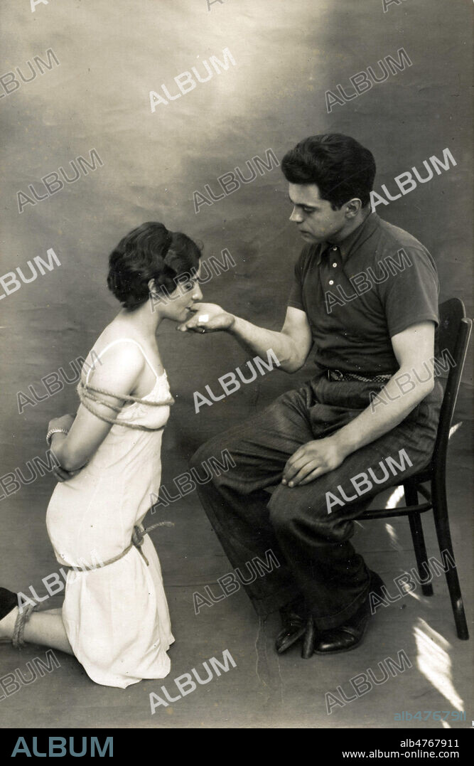 Femme soumise attachee : les membres attaches, elle mange du sucre dans la main d'un homme (comme un chien). Photographie erotique anonyme pour une carte postale vers 1930. Credit : Collection IM/KHARBINE-TAPABOR.