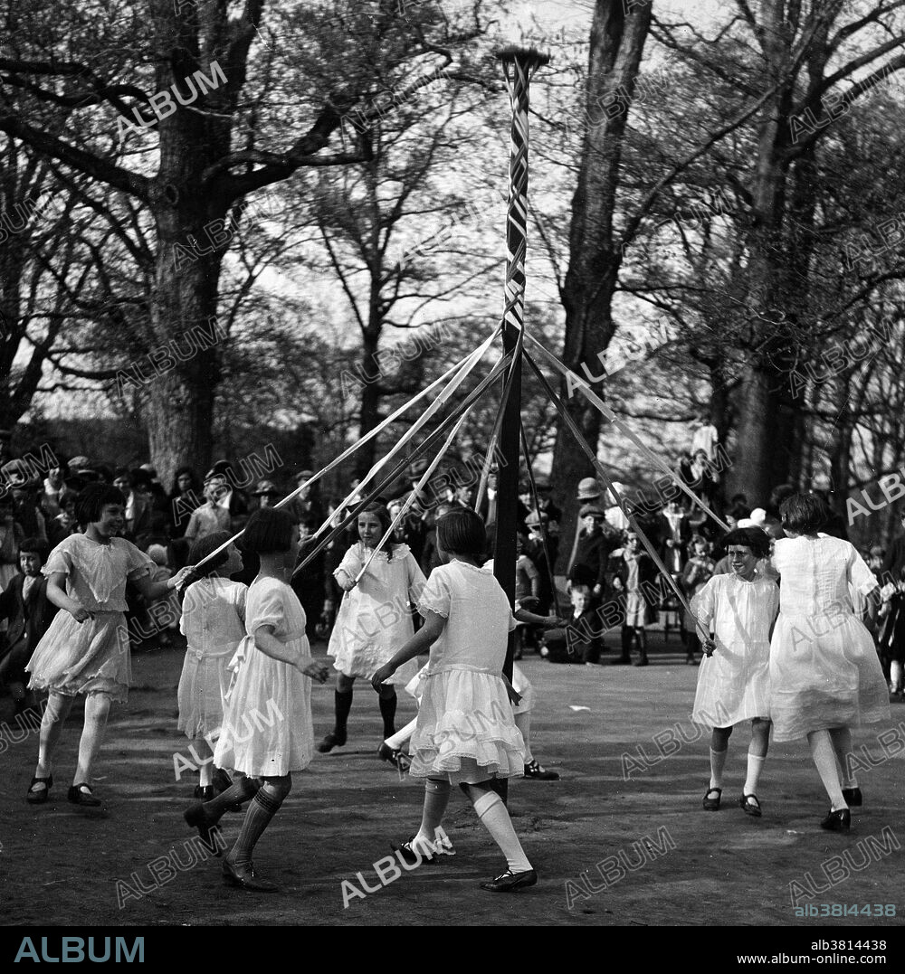 Entitled: "Playgrounds, May Day. May pole dance." Maypole dancing is a form of folk dance from Germany, England, and Sweden. The most popular maypole dance consists of dancers that perform circle dances around a tall, garland-festooned pole (originally a live tree).The dancers move in a circle, each holding a colored ribbon attached to a much smaller pole. As they move around the pole, the dancers intertwine their ribbons either in a web around the pole or to plait it to the pole, itself. To unravel the ribbons, the dancers retrace their steps. Historians believe the first maypole dance originated as part of Germanic pagan fertility rituals. While dancers usually perform this dance in the spring on May 1 or May Day, those in Sweden perform it during their midsummer celebrations. Photographed by Harris & Ewing, 1924.