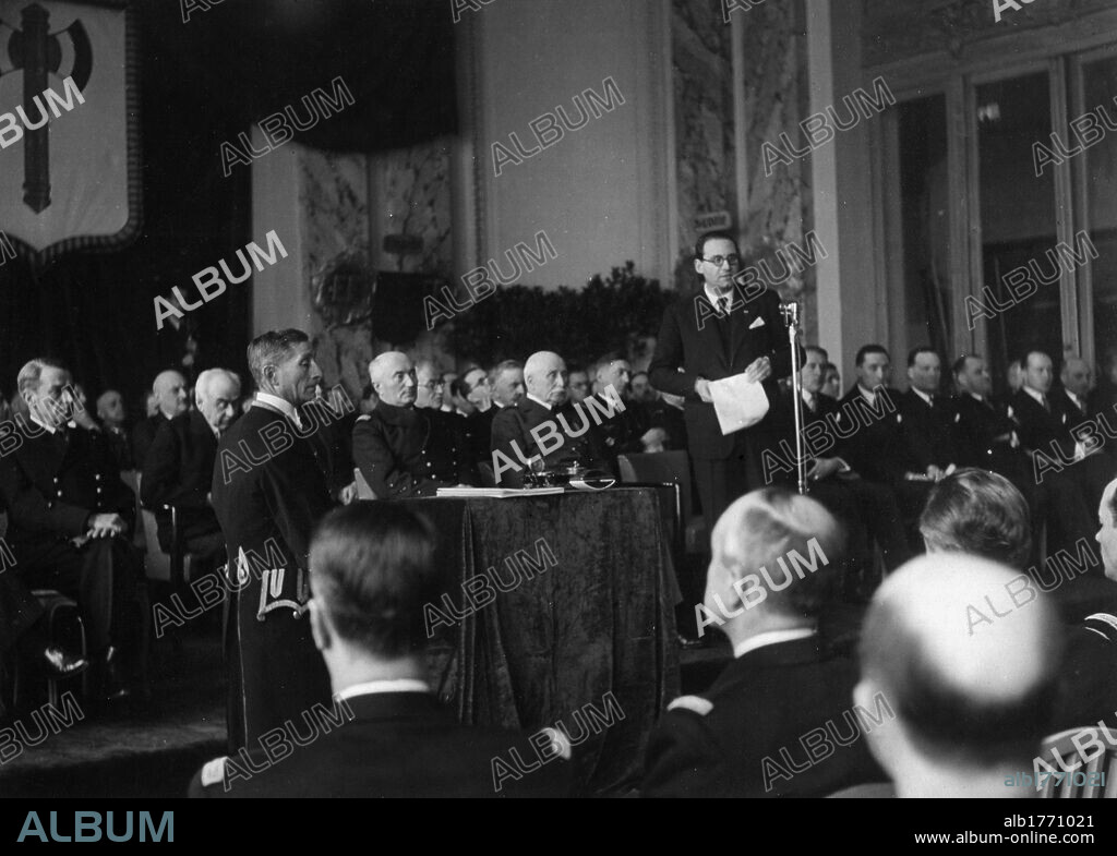 Pierre Pucheu delivering a speech in the presence of Philippe Petain. In the hall of honour of Vichy town hall, the Minister of Interior Pierre Pucheu delivering a speech for the oath ceremony of the Government of Vichy, in the presence of the admiral and Vice-president of the Council of Ministers Jean Louis Francois Darlan and the Marshal and Chief of the French State Philippe Petain. Vichy, 19th  February 1942.