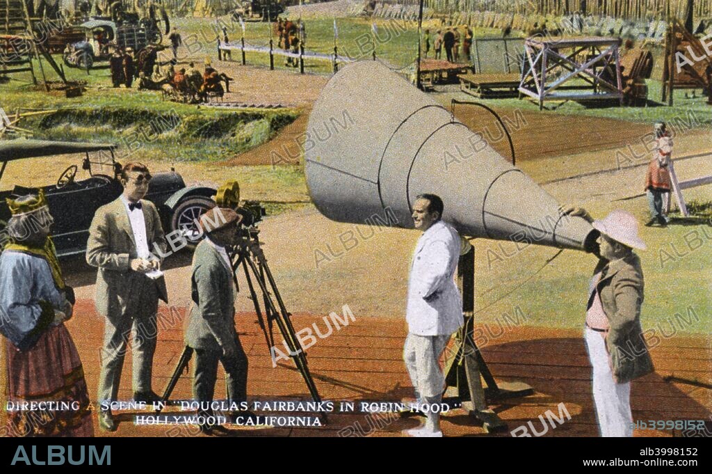 Directing a scene on a film set, Hollywood, Los Angeles, California, USA, 1922. During the filming of 'Robin Hood', starring Douglas Fairbanks. Vintage postcard showing a movie lot with sets in the distance. In the foreground a director and others talk to the actors.