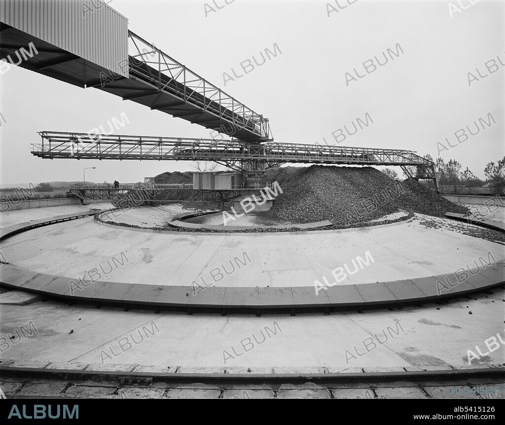 JOHN LAING PLC. Sugar beet in the polar beet silo at Wissington Sugar Factory, showing the conveyor bridge, shuttle convey and water jet system. A sugar factory was first built at Wissington in 1925. Work began on the construction of a new refinery, five silos, and an extension to the existing factory in March 1968 for the British Sugar Corporation. The project also involved the realignment of railway sidings and was spread over three and a half years. Work was programmed to align with the sugar beet campaign: between September and February each year the focus of construction work shifted from the factory to the silos and other outer works, allowing the factory to open for the unloading and processing of sugar beet. At the time of its construction, the polar beet silo at Wissington was the only one of its kind in England. Beet was unloaded from lorries and entered the silo via the conveyor bridge, and was then distributed by the shuttle conveyor. The base of the silo formed concentric valleys with flumes leading to catchment troughs which carried beet to the factory.