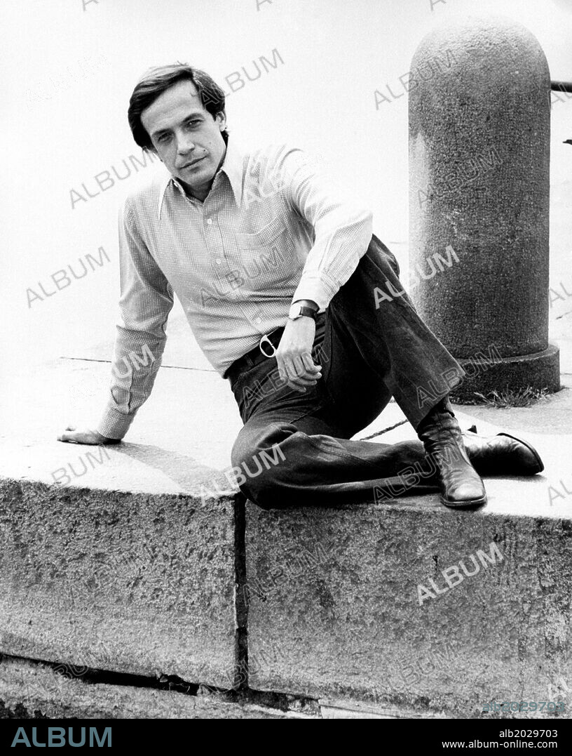 Roberto Bisacco posing on a small city wall. The Italian actor Roberto Bisacco in his hometown, sitting in pose on a small wall of Lungo Po. Turin (Italy), 1975.