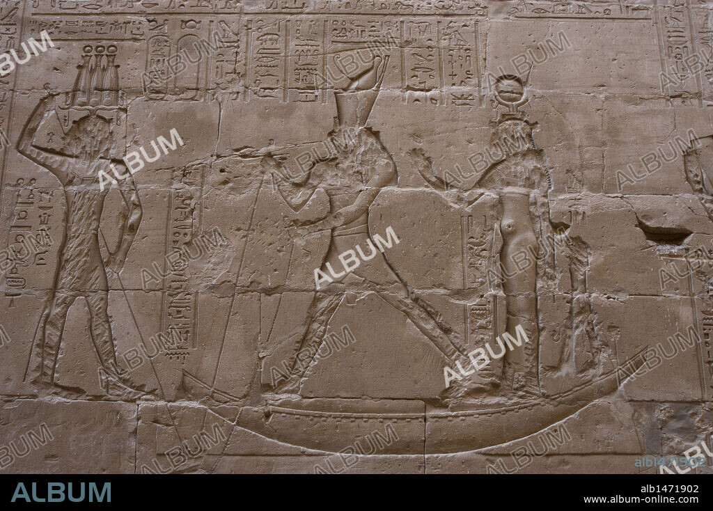 Arte Egipcio. Edfu. Templo de Horus. Siglo III A. C. Relieve que representa al dios Horus, de pie en un barco, en batalla como venganza por el asesinato de su padre por su tio el dios Seth, sosteniéndolo con cadena y lanza bajo el agua y representado por un hipopótamo. Detrás, la diosa Isis y Horus Khenti-Khatti. Corredor exterior.