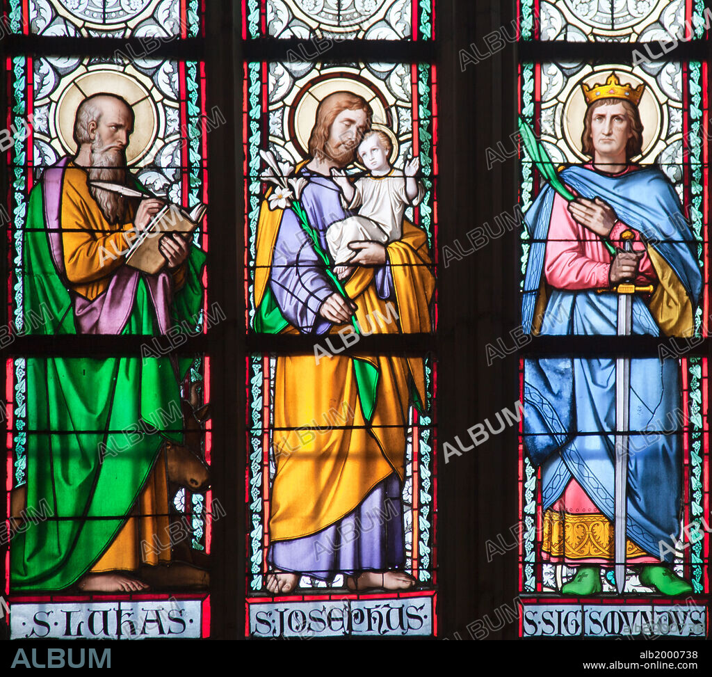 Prague, St. Vitus Cathedral, Stained Glass Window, St. Luke, St. Joseph, St. Sigismund. Part of a Stained Glass Window depicting (from left to right) the standing figures of St. Luke writing in a book, St. Joseph holding baby Jesus and some flowers, and St. Sigismund, who was also a king, holding a sword and a branch.