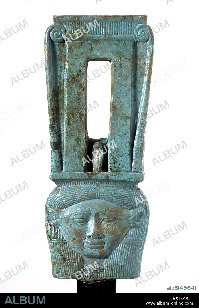 Sistrum in Naos form with depiction of the goddess Hathor, Faience, hand modeled, pressed into the form, Faience, Quartz ceramics, Total: Height: 17 cm; Width: 7 cm; Depth: 2.7 cm, Musical instruments, ritual objects and accessories, Temples and sanctuaries (Egyptian religion), Head, face, antiquity, The sistrum is a rattle that was used in the cult in Egypt and Mesopotamia This faience sistrum has an identical design on both sides: Above the head of the goddess Hathor - recognizable by her cow ears - rises a slender construction (naos) with a hollow at the top and a Uraeus snake on the threshold. On the sides, volutes rise, their snails are inserted into the hollow at the top. The inside of the naos appears as a rectangular slit in which the rattle discs could move. Three holes for the rattle bars are inserted in the sides. On the flat upper side there might have been a figurative attachment. The base of the rounded handle can be seen at the bottom.