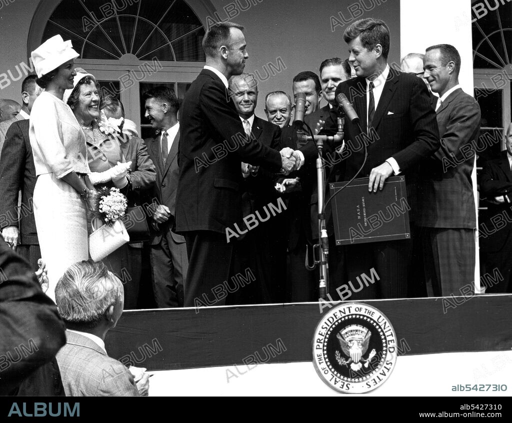 Kennedy and Shepard in Washington D.C., 1961. President John F. Kennedy congratulates astronaut Alan B. Shepard, Jr., the first American in space, on his historic May 5th, 1961 ride in the Freedom 7 spacecraft and presents him with the NASA Distinguished Service Award. The ceremony took place on the White House lawn. Shepard's wife, Louise (left in white dress and hat), and his mother were in attendance as well as the other six Mercury astronauts and NASA officals, some visible in the background.