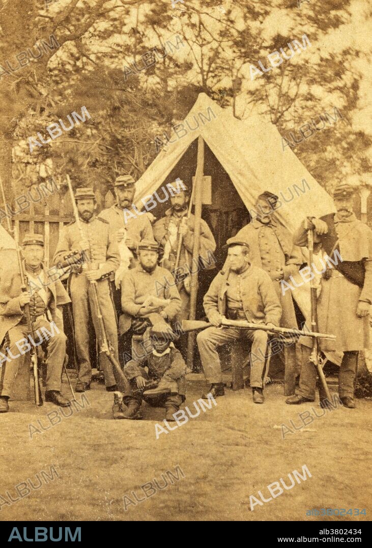 Life in Camp Cameron, Washington, DC. Photograph shows uniformed soldiers with guns posed in front of a tent; an African American child sits in front of the group. Photo by Mathew Brady studios, 1861.