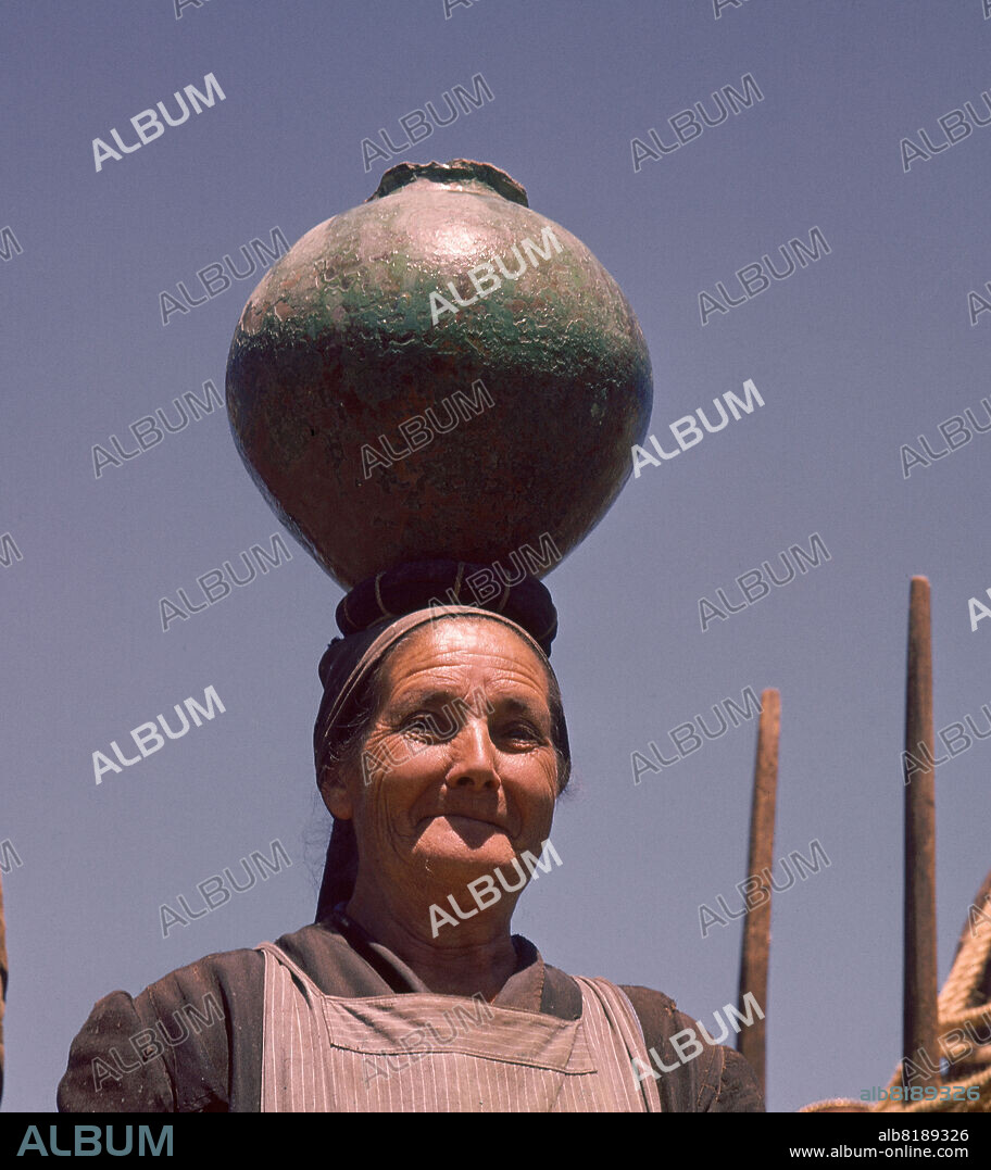 MUJER LLEVANDO UN CANTARO EN LA CABEZA CON RODETE - FOTO AÑOS 60.