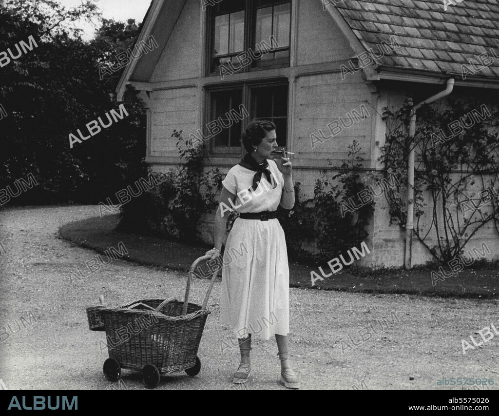 The Duchess Of Kent And Her Daughter, Princess Alexandra - The Duchess of Kent with wicker-work gardening trolley, pauses to smoke a cigarette while waiting for her daughter. September 7, 1954. (Photo by Michael Mckeown).