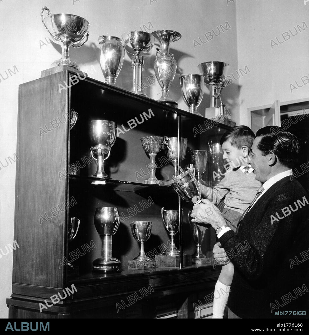 Fausto Coppi with his son Angelo. Italian cyclist Fausto Coppi showing his son Angelo Fausto some trophies that he won. 1959.