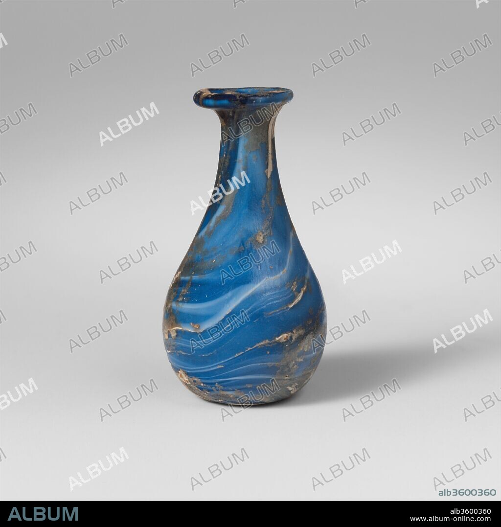 Marbled glass perfume bottle. Culture: Roman. Dimensions: 2 3/8 × 1 1/4 in. (6.1 × 3.2 cm)
Lip diameter: 3/4 in. (2 cm). Date: early to mid-1st century A.D..
Translucent blue and opaque white.
Rim folded out, over, and in, and smoothed into sides of flaring mouth; short, cylindrical neck, expanding downwards to join imperceptibly with ovoid body; flattened, slightly concave bottom. Numerous trails applied to gather and marvered into surface, forming an irregular way pattern extending from rim to bottom.
Intact; some bubbles; deep pitting, dulling, and patches of iridescence and creamy white weathering.
Oval blue and white blown glass marbled perfume bottle.