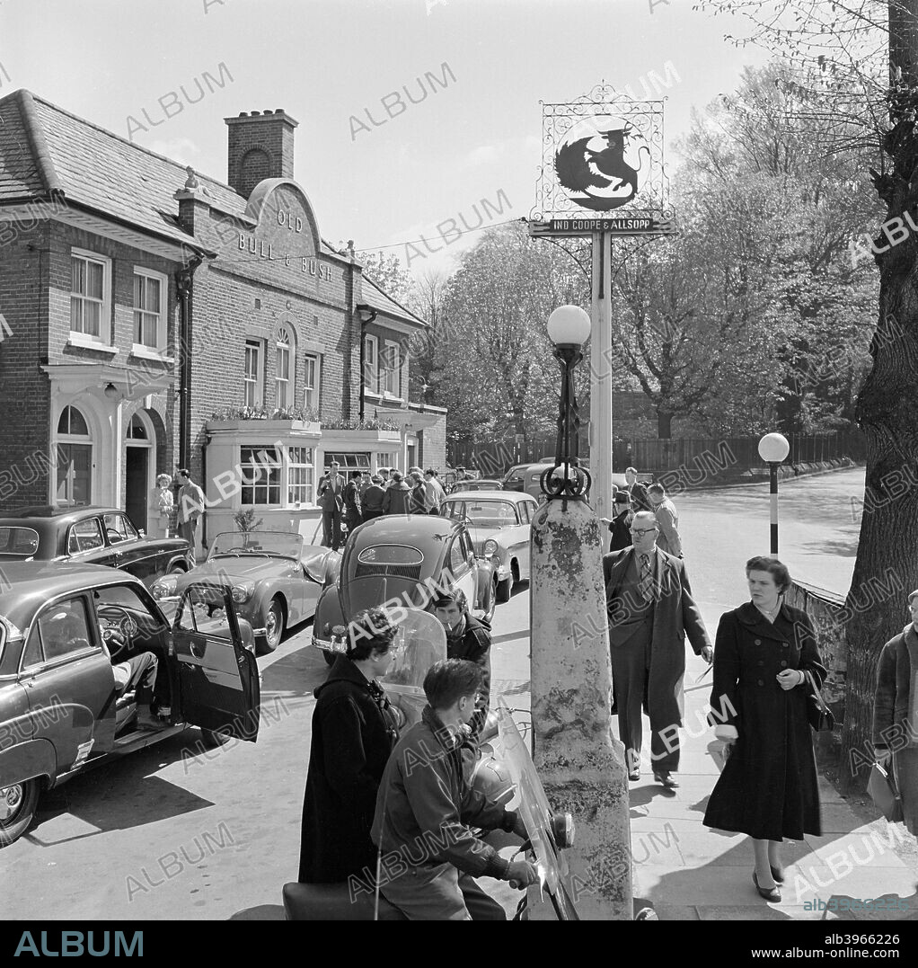 The Old Bull And Bush public house, North End Way, Hampstead, London, 1962-1964. The road outside the Old Bull and Bush crowded with people and cars, two lads on scooters in the foreground watched by disapproving passers-by.