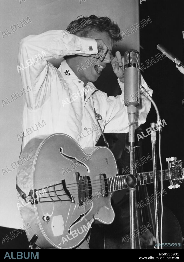 Orig. bildtext... TONÅRSIDOLEN TOMMY STEELE gästade på måndagskvällen Anglais-teatern som var fylld till sista bänk med rock'n roll fantaster. På bilden är han tvungen att torka svetten ur ögonen vilket man kan tro hör till programmet. Anm. Gnugga sig i ögonen Gitarrer Idoler Gapa persons: TOMMY STEELE sites: STOCKHOLM;SVERIGE;STORBRITANNIEN*.