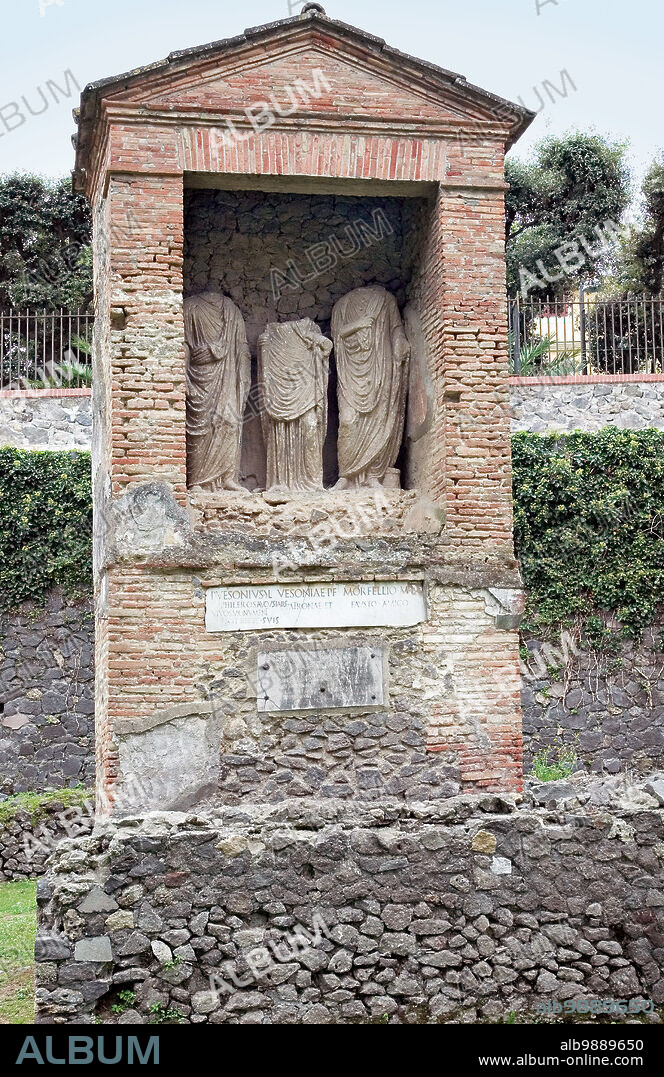 Funeral Monument of Vesonius Phileros. Funerary monument of Vesonius Phileros, late 1st century BC-early 1st century AD. Italy, Campania, Pompeii, necropolis of Porta Nocera. Total. In the aedicule are three tufa statues, the central female, the lateral male. Two inscriptions are visible: in the first higher up it is specified that the tomb was made, while he was still alive, by P. Vesonius Phileros, augustale, a freedman of Vesonia, for himself, his wife and his friend Marcus Orfelius Faustus. The second slab, embedded in the stucco of the facing and added at a later time, reads, "Passenger, stop a little, if it does not inconvenience you, and know what you should beware of. He (whose name is inscribed) whom I hoped was my friend, falsely accused me. In judgment, by the grace of the gods and my innocence, I was freed from all harassment. May he who slandered me be rejected by the penitent gods and those of the underworld.".