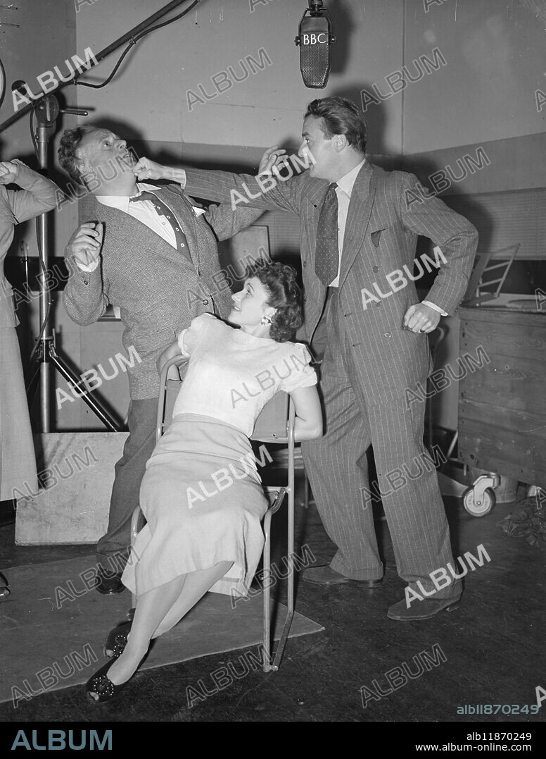 ' ONE UP TO DICK '. Although DICK BARTON appears to be setting about that dangerous villain , FLASH FARADAY , in no uncertain style it's fairly safe to assume that Dick's mighty punch is being pulled - this dramatic incident is only a rehearsal for next week's B.B.C. Serial thriller 'The J.B Case' with Noel Johnson as Dick and Sydney Vivian as Flash. The charming girl in the chair is Violet Loxley who plays Freda , the heroine. The play is by Edward J J Mason , Produced by Neil Tuson, and should add to Dick's already considerable reputation. September 16 1948.
