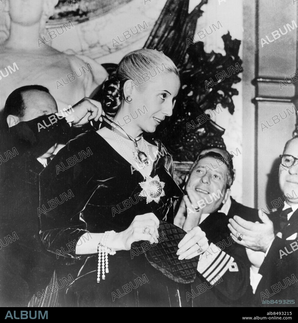 Orig. bildtext... NEW HONORS FOR EVA PERON BUENOS ARGENTINA.....MRS. EVA PERON, ATTRACTIVE WIFE OF ARGENTINE PRESIDENT JUAN PERON IS SHOWN BEING DECORATED WITH THE OMEYADES ORDER DURING A RECENT CEREMONY IN BUENOS AIRES. A MEMBER OF THE SYRIAN DELEGATION IN ARGENTINA IS ATTACHING THE RIBBON OF THE ORDER AROUND MRS. PERON'S NECK AS HE MADE THE PRESENTATION IN HIS COUNTRY'S NAME. Anm. Perón, Eva, 1919-1952, argentinsk politiker Armband Halsband Pärlor Clips Öronclips Ringar Handväskor Leenden Gradbeteckningar Utmärkelser Officerare Kraschaner Societet Hedersbevisningar CD403 persons: EVA PERÓN sites: SYDAMERIKA;SYRIEN*;ARGENTINA;BUENOS AIRES.