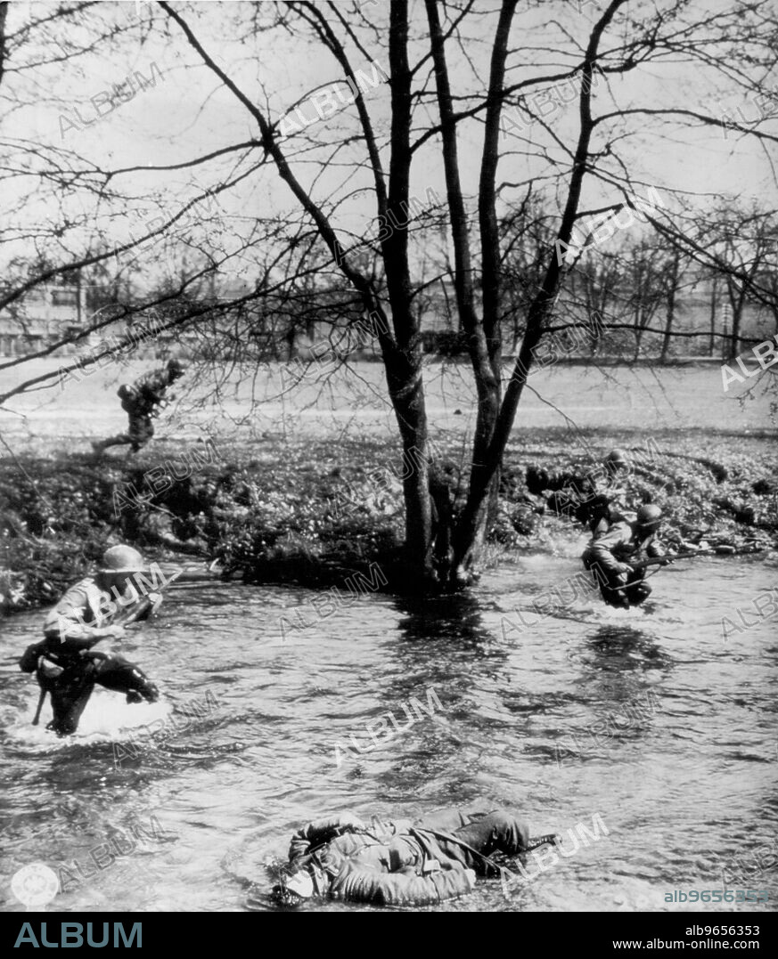 Yanks Stream past Dead SS Trooper -- Cut down by a Machine Gun burst, a Dead German SS trooper lies in the Schleuse river near Waldau, Germany, as Yanks of the 26th division splash by to ford the steam and attack enemy positions in nearby pine Forests. April 18, 1945. (Photo by AP Wirephoto).